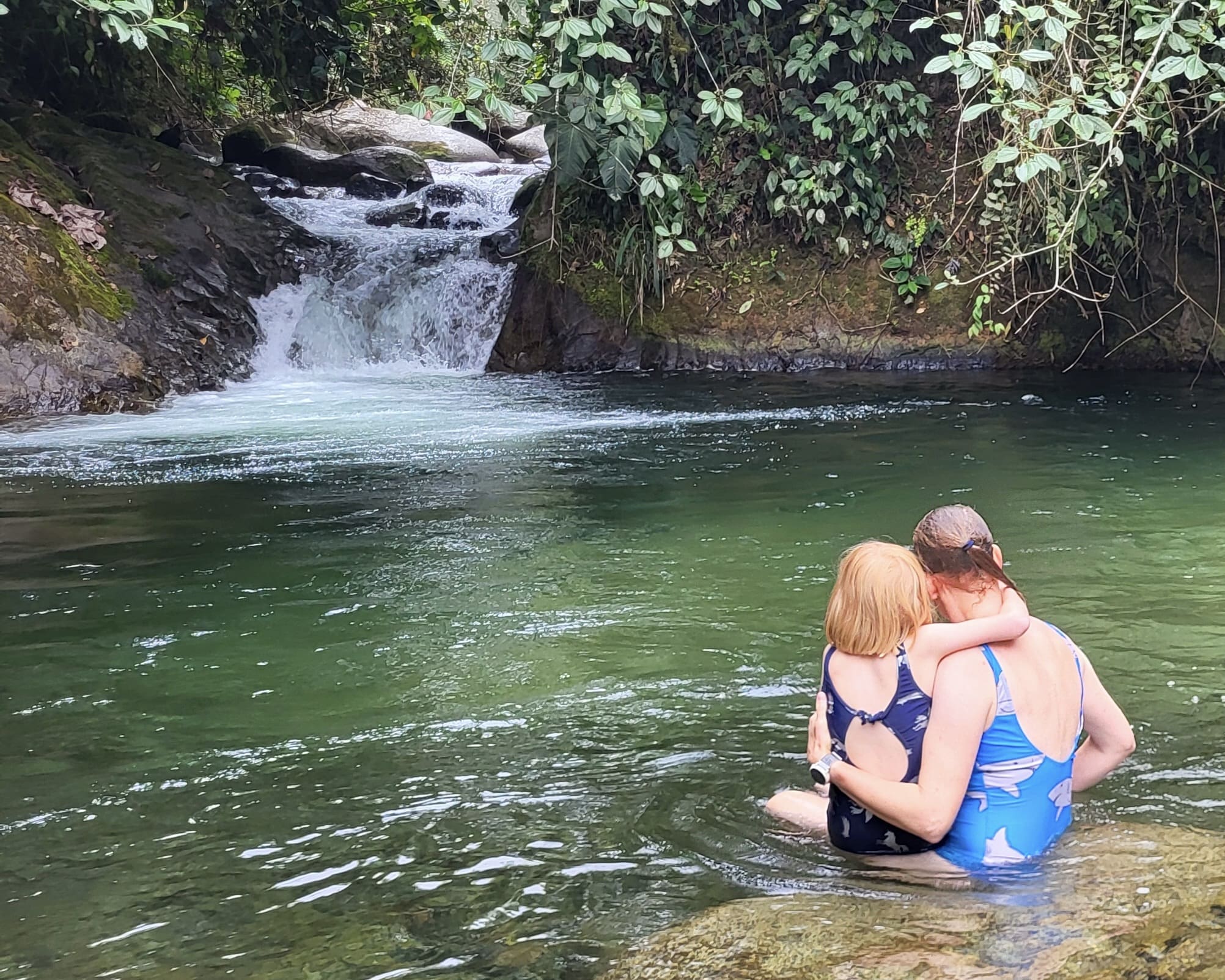 A mother and daughter sit in a natural swimming hole, hikable from Eco Cabañas Junin.