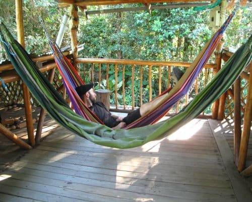 A man relaxes in a hammock on a shaded porch